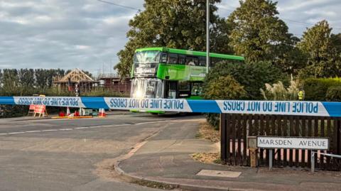 A green double decker bus behind a police cordon