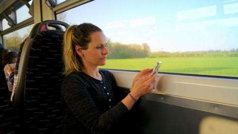 A woman sits alone on a speeding train reading from her mobile phone.