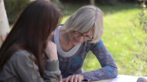 A woman pointing to words and reading it to another woman