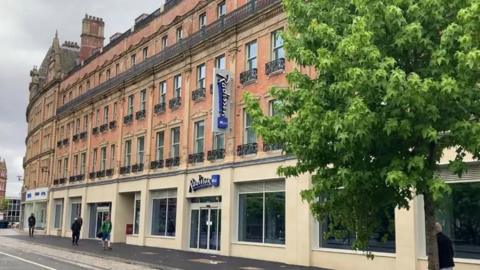 The outside of a hotel with an ornate, red brick, Victorian facade and black iron balcony railings