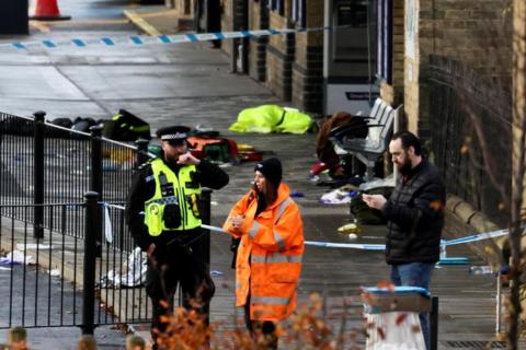 A police officer and another woman wearing high-vis along with a man in plain clothes stand in front of a cordoned section of the pavement - objects lie on the ground