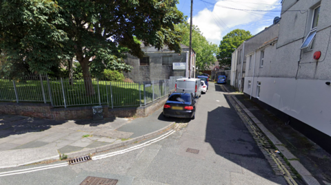 A Google street view of Belmont Street in Plymouth. Cars are parked up on the pavement with garages visible in the back of the photo.