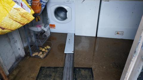Sewage pictured in a garage. The sewage can be seen on the floor alongside two planks leading to the washing machine.