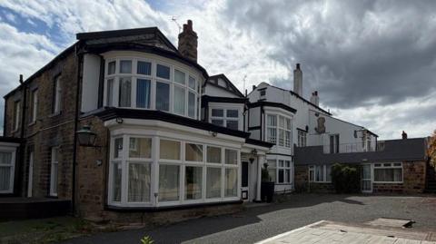 A brick building with bay windows - a large but slightly run down house.