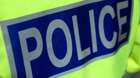 A police officer's high visibility jacket. The word "police" is in silver letters on a blue background.