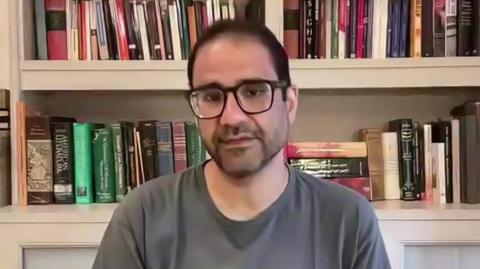 Alaa Abdel Fattah speaks via video link to the BBC in October 2025, sitting in front of a bookshelf and wearing a grey T shirt