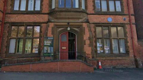 A red brick Gothic building in a picture taken from Google Street View. It has a large red door which is open for visitors.