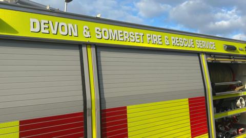 The side of a Devon and Somerset Fire and Rescue fire engine. Yellow and red hi vis sticks are on the outside of the vehicle. A Devon and Somerset Fire and Rescue Service sign is above the door.