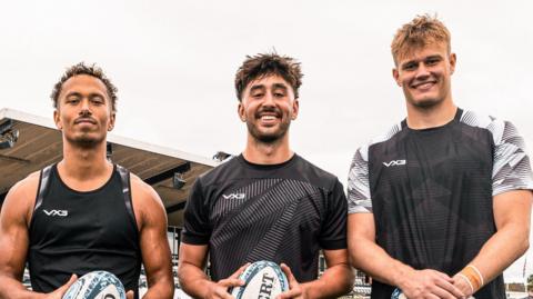 Harrison Obatoyinbo (left), Joel Grayson (centre) and Sam Waugh (right) all holding rugby balls as they look at the camera