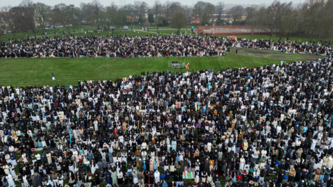 A drone view of Muslim men and women praying in a park.