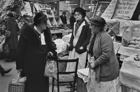 Merched yn sgwrsio ger stondin bara lawr ym Marchnad Caerdydd yn 1939