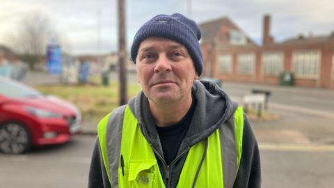 Robert Morley wearing a black beanie hat and a yellow high visibility jacket on top of a grey hoodie.