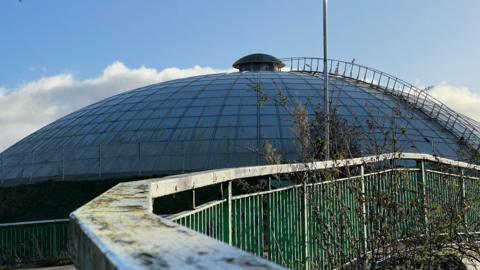 A large domed building that has been neglected with peeling railings on a  footpath leading up to it