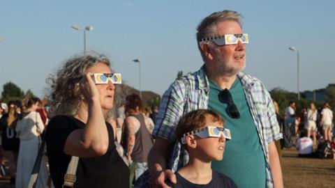 Woman, man and child staring at the sun.