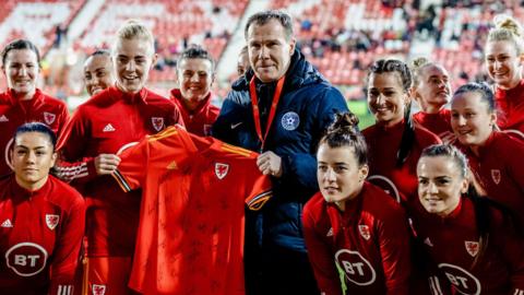 Jarmo Matikainen poses holding a Wales shirt with members of the Wales team