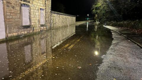 A flooded road in the dark. The road is illuminated by street lights.