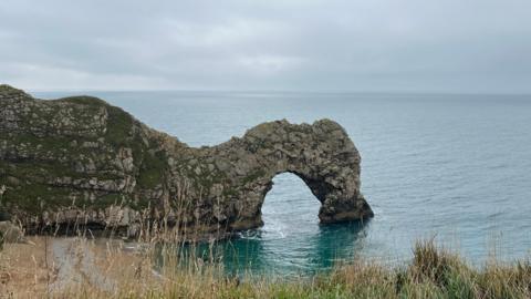 Durdle Door - a natural rock arch over a body of water in Purbeck - surrounded by greenish-blue water and under a cloudy sky