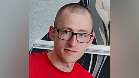 Martyn Richardson wearing a red top and black framed glasses.