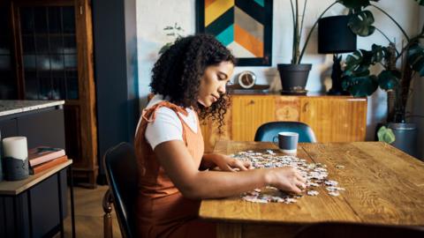 Woman building a jigsaw puzzle on a dining table.