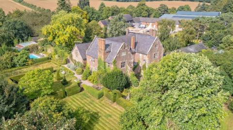 An aerial view of a large Elizabethan house, surrounded by green fields and woodland