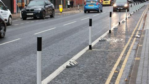 A section of the Linthorpe Road cycle lane which is marked by a solid white line and black and white poles. Cars can be seen to the left of the cycle lane.