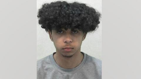 A mugshot of Leandro Lopes. He has thick, curly black hair. He has a short beard under his chin and light hair on his top lip. He is wearing a grey T-shirt.