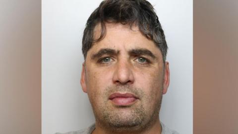 Mugshot of Nathan Cooper, who has wavy dark hair and is wearing a grey top.