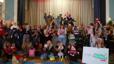 A picture of around thirty mums and babies from the "Pramlife" video with The Everly Pregnant Brothers and local singer Kia on the stage behind them.