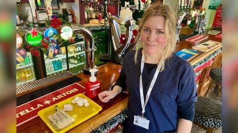 A nurse stands at the bar of a pub with flu vaccination equipment.
