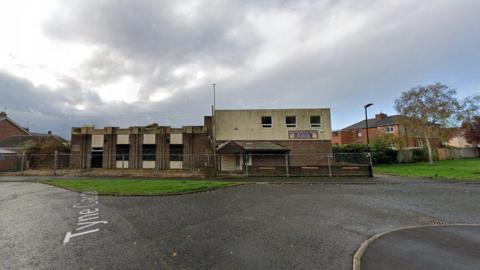 A derelict detached building with metal fences surrounding it.