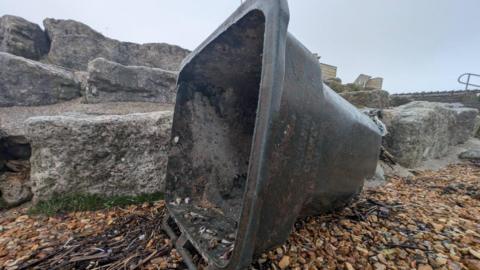 A black bin washed up on a beach with the words Baldwin County Alabama on it.