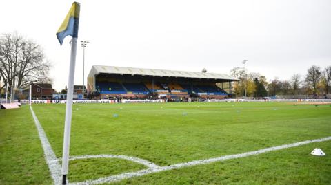 The Walks Stadium in King's Lynn where King's Lynn Town FC trains. In the picture is a green pitch with spectator stands.