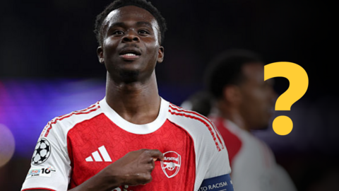 Bukayo Saka pointing to an Arsenal badge on his shirt