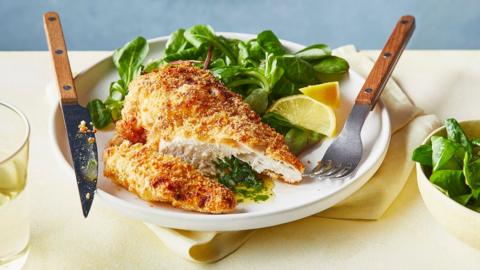 Chicken kiev on a bed of spinach on a circular plate with a knife and fork