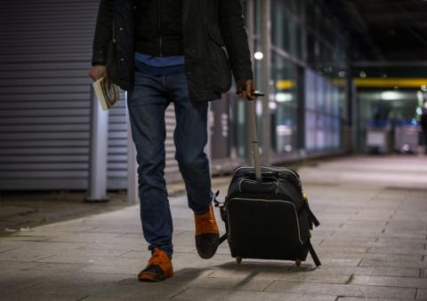 A passenger wheels a suitcase while walking out of the airport. 