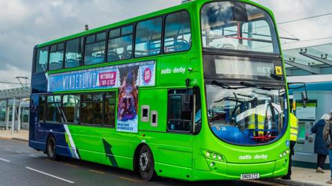 A bright green Notts+Derby double decker bus parked outside of a bus station in Derbyshire