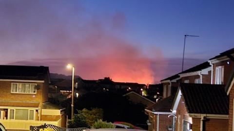 A glow from the blaze, beyond a number of houses