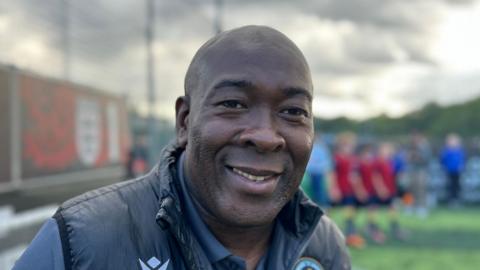 Man smiles at camera, he is wearing a dark jacket and shirt