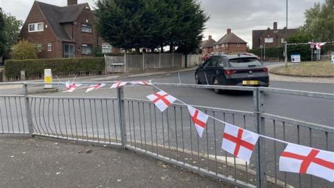 A string of flags on a roundabout. In the background is a black car