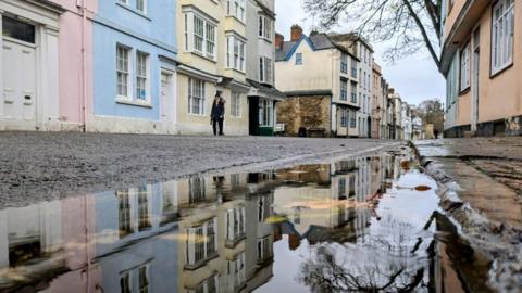 Flooding on road with cobbled pavement and pastel homes either side.