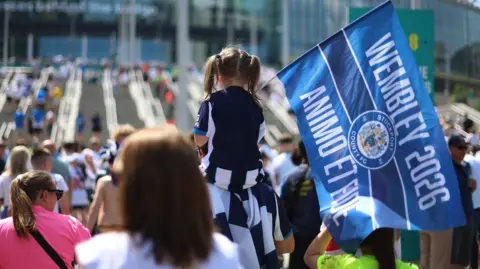 Young Stockport fan holding a flag on top of man's shoulders on Wembley Way