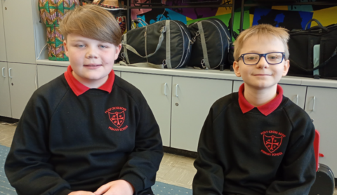 Jake on the left has sandy hair parted to the side while Jack has short fair hair and black-framed glasses. Both are wearing black Holy Cross sweatshirts with red shirt collars visible