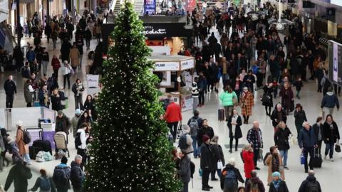 Crowds walk in a railway station next to a large Christmas tree.