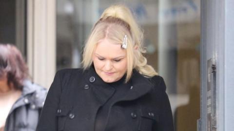 Hollie Dance leaving Southend Crown Court wearing a black coat. She has long blonde hair.