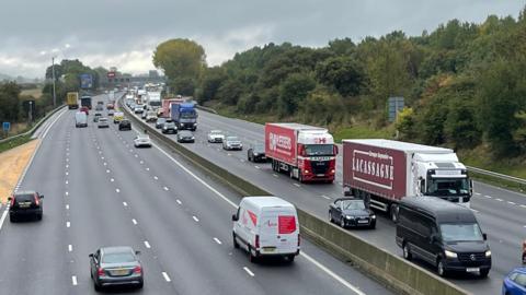 A view of traffic on the M6 with queues in the distance, near a bridge and a junction sign