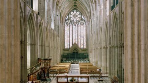 The nave of Worcester Cathedral shows a tall stained glass window with stone arch walls