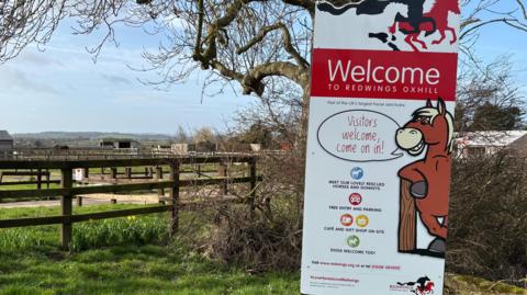 The welcome board to Redwings Oxhill in south Warwickshire shows a cartoon horse saying 'Visitors welcome, come on in!'.