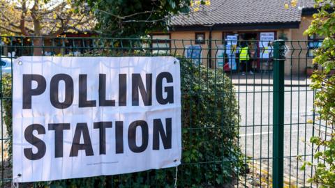 A white sign on a school fence indicating it is a polling station