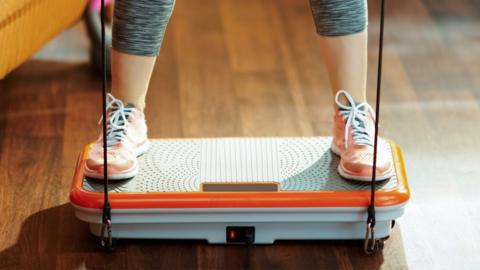 Two feet standing on a vibration plate on a laminate wooden floor.