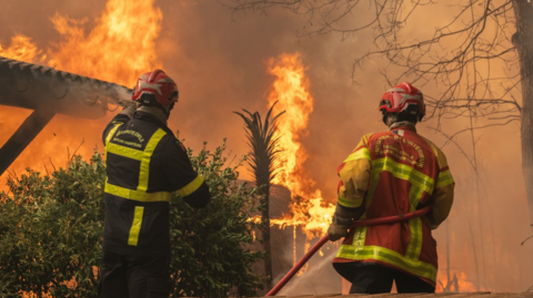 Firefighters battle a blaze at a house damaged in wildfires in France.